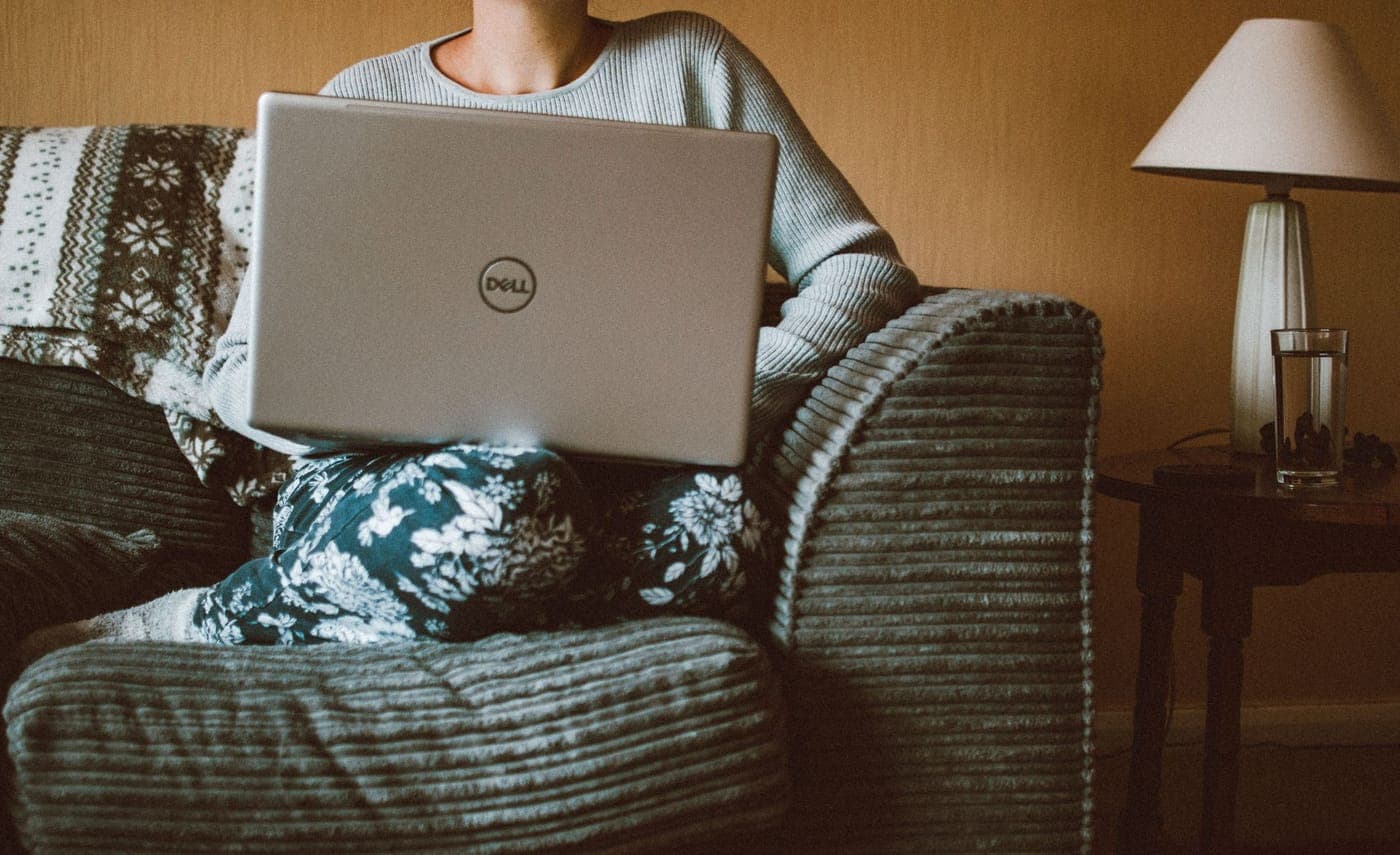 Iemand werkt thuis op de bank met een laptop op schoot